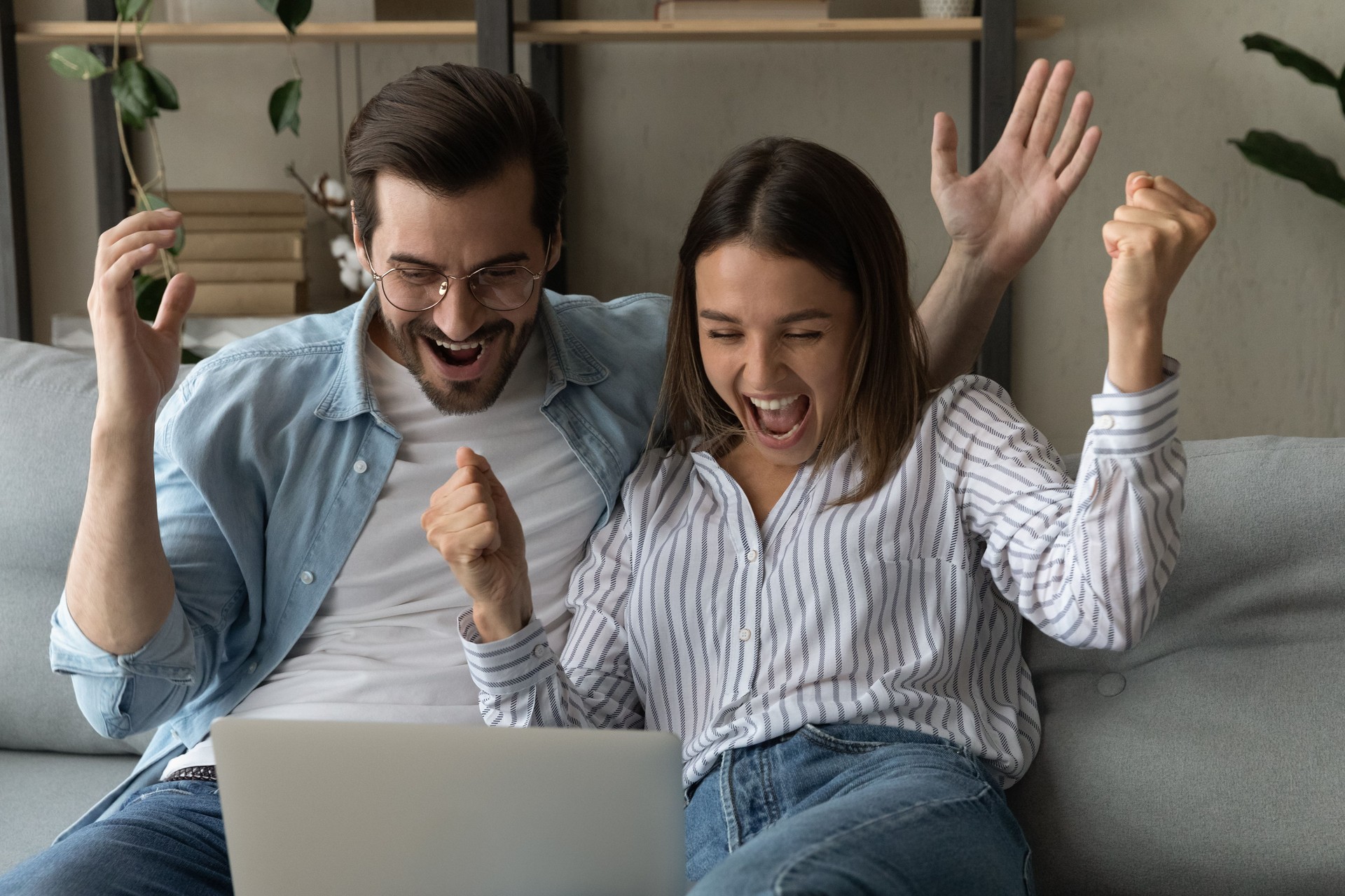 Euphoric couple read unbelievable news on laptop celebrate success Euphoric couple read unbelievable news on laptop celebrate success
